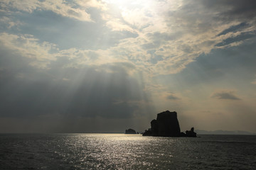 Obraz premium Sun rays shining on small deserted island in Andaman sea near Phi Phi, showing only silhouette of rock. Ao Nang, Thailand