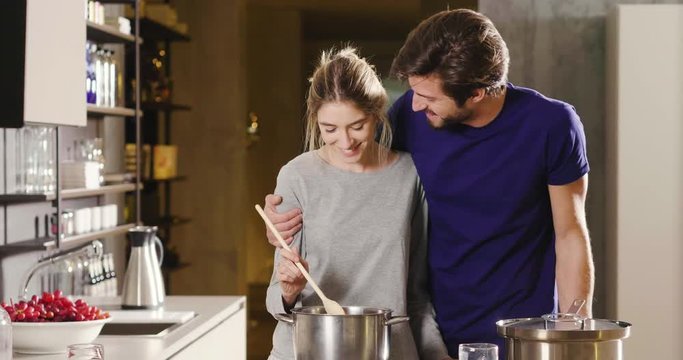 An engaged couple cook together and have fun while tasting the sauce they have prepared. The married couple embraces to show their love. Concept of: cooking, love, lifestyle.