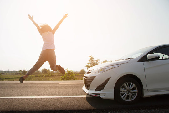 Asian woman happy jump with car on road and sunlight
