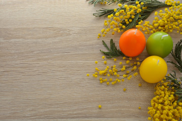 Religious international Easter holiday - candles in the form of colorful eggs, flowers (mimosa) and bright morning light.
