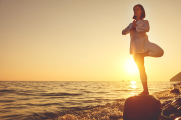Fototapeta na wymiar woman practices yoga and meditates on sunset beach