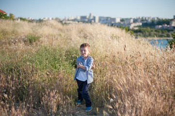 Naklejka na ściany i meble funny cute little boy grimacing standing in the middle of a field of plants in summer