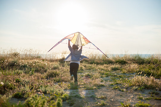 sport little kid with kite in his hands running towards summer sea horizon