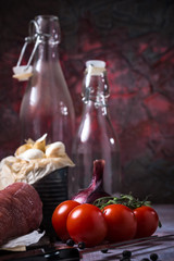 Red tomatoes next to whole pork tenderloin meat on vintage board and garlic