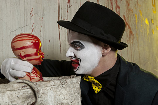 evil clown playing with bloody doll