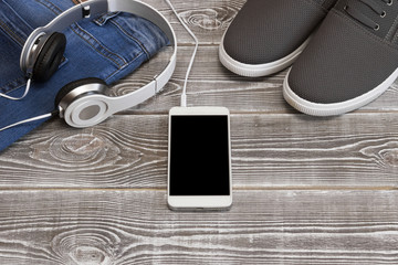 Jeans headphones smartphone sports shoes on a wooden background. active lifestyle recreation.