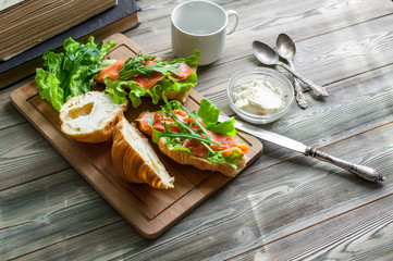 The fresh baked croissants with butter, a salty salmon and leaves of arugula on a chopping board on a wooden table. Breakfast concept