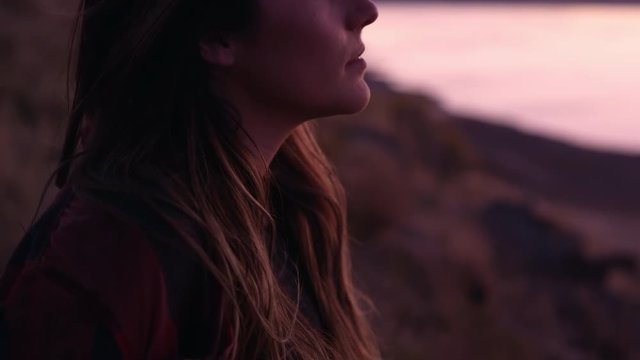 Slowly panning up to young womans face at sunset as she looks off into the distance.