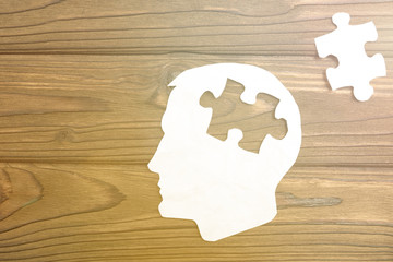 head of a man from a paper on a wooden background. puzzle piece. think. idea. business vision.