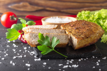 fried meat with tomatoes and greens on a black stone