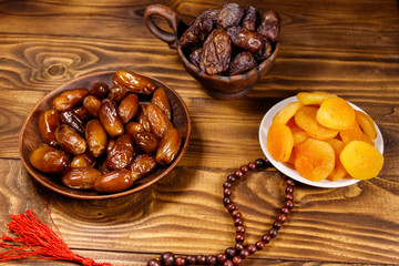 Fototapeta premium Dried apricots and dates fruit with wooden rosary on wooden table
