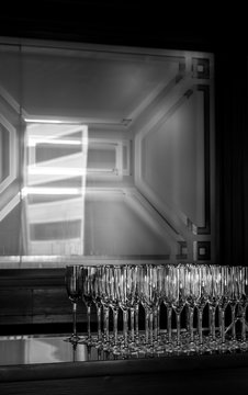 Clean wine glasses sit shimmering on a bar in the lower right side. A geometric pattern in embedded in the mirror and window is reflected in the bar's mirror. Vertical image in black and white.