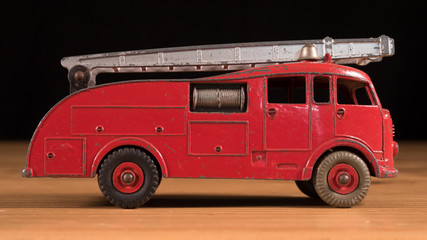 Old retro metal toy fire truck on wooden table with black background