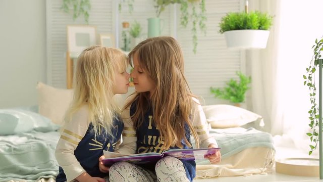 Two little girls in a bright room with plants, read a book