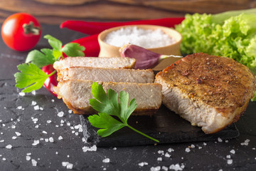 fried meat with tomatoes and greens on a black stone