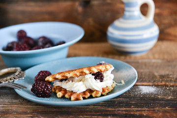 Round waffles with fresh blackberries and whipped cream, on natural wooden background in rustic style