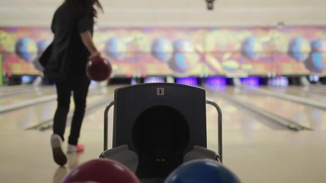 Young Man In Bowling Lane. Male teenager with a long hair chooses a bowling ball and throws it