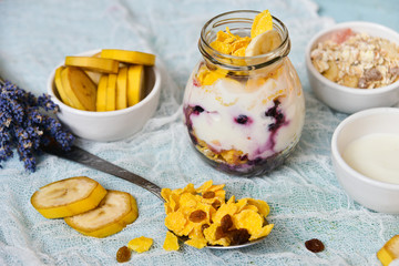Breakfast in a glass jar: homemade granola, banana, fresh berries, yogurt on a light textile background with a bouquet of lavender. The concept of healthy eating, high-carbon Breakfast.