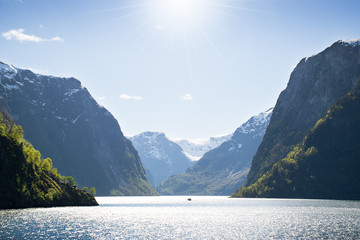 Norwegian landscape with sunbeams above the water among the mountains and with a small ship in the center