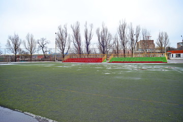 Football field and tribune with snow and puddles on the field