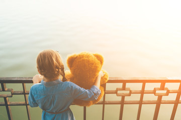 Girl embracing a cute teddy bear looking to water