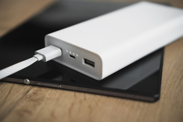 White power bank with tablet pc on wooden surface.