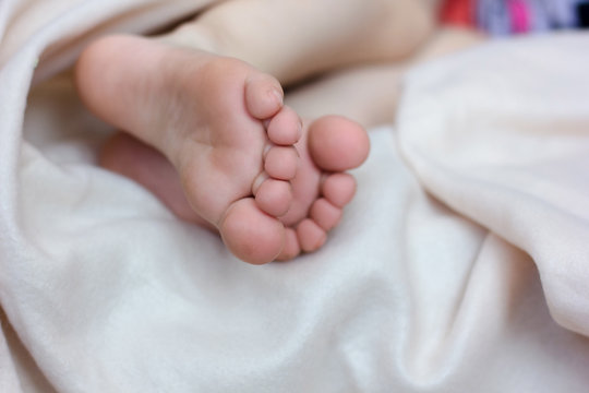 Kid laying in the bed and foot with toes and heels on white blanket.