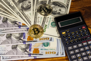 Fototapeta premium Two bitcoins, calculator and one hundred dollar bills on wooden desk