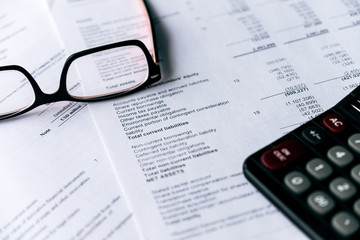 Investment and Financial analysis and reporting concept, Calculator and eyeglasses lying on financial performance report.