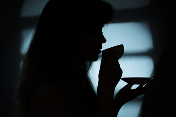 silhouette of a girl near a window with a cup of hot drink