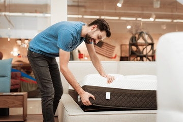 Young bearded man is testing mattress in furniture shop. Orthopedic mattress for a healthy posture.