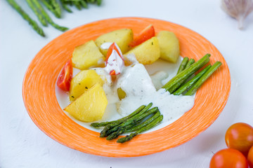 Potatoes and asparagus with tomatoes and tartar sauce on plate ready to eat.