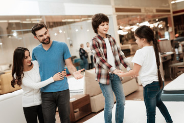 Young couple looks like children are jumping on mattress in furniture store. Happy family choosing...