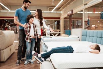 Blissful family buys new orthopedic mattress in furniture store. Happy family choosing mattresses...