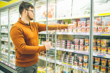man takes yogurt from fridge. grocery shopping concept