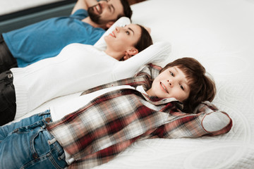 Young beautiful couple with cute little boy lies on bed in mattress store.