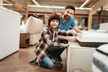 Bearded man with young son is testing mattress for softness. Testing softness of mattress.