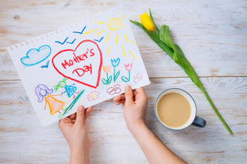 mother look on kid picture with mother day congratulation while drink coffee. overhead view
