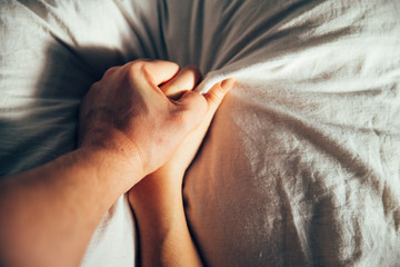 man squeezes woman hand on white sheets. Passion while making love