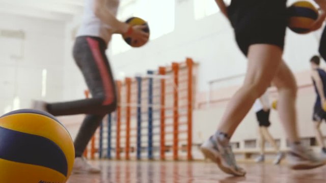 School Volleyball Training. Boys and girls are running in the gym and twist balls around themselves. One of them lost the ball and lagged behind. Later he caught up the others.