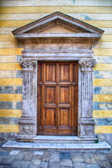 Medieval ancient wooden door with ornate stone columns, Italy.