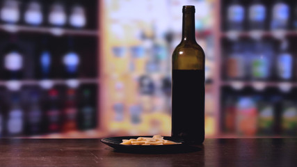 A bottle of red wine, cheese, a background bar counter.