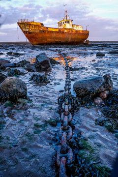 Rusty old fishing vessel marooned at low tide on a mud bank a long anchor chain