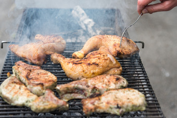 Man fry steaks and chicken thighs on the grill, rest with friends in the open air