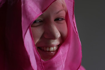 Young blonde girl portrait with head covered with a pink silk scarf. Smiling happily.