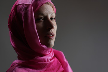 Young blonde girl portrait with head covered with a pink silk scarf. Looking boldly.