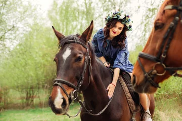 Foto op Canvas a girl in festive clothes and with a wreath on her head sitting on a horse and touching it with her own hand © Ivan