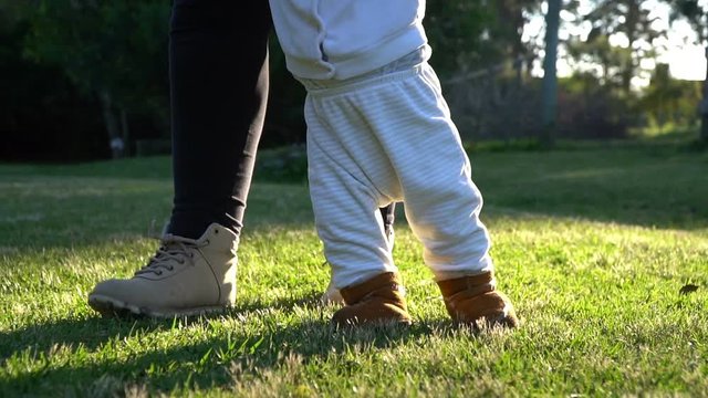 Baby boy walking first steps with mom outside