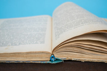 Close up opened vintage retro book page with blurry text for education and publication concept on blue background. Focus on book binding. Knowledge, studies, learning, university concept