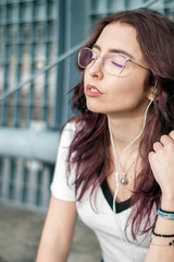 Beautiful young woman listening to music through white earphones at outside scene